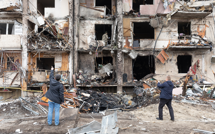 Two men standing in front of destroyed apartment building in Ukraine